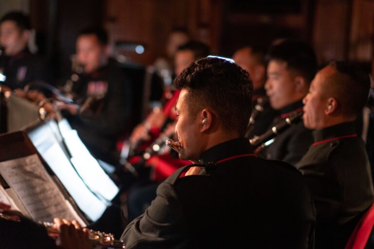 A group of musicians in uniform performing in an indoor setting with wind instruments.